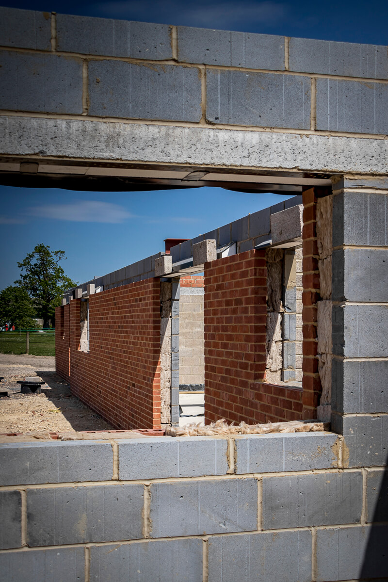 Structural blockwork and facing brickwork are rising rapidly, transitioning this high-end residential build from a ground-level footprint into a highly defined, physical space. The perimeter and internal partition walls are quickly taking shape, establishing the core layout and rooms of the property.